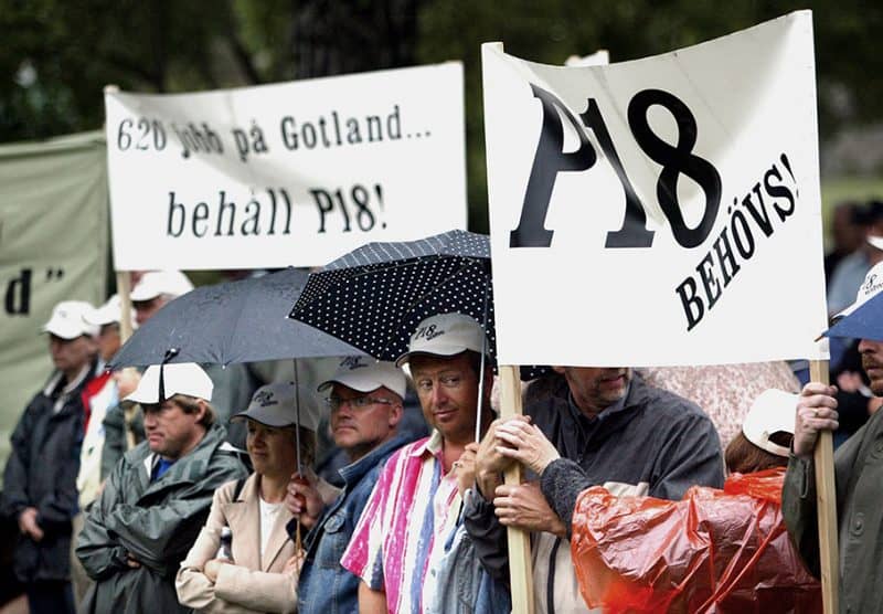 En grupp människor står med plakat med texten"620 jobb på Gotland... behåll P18" och "P18 behövs!"